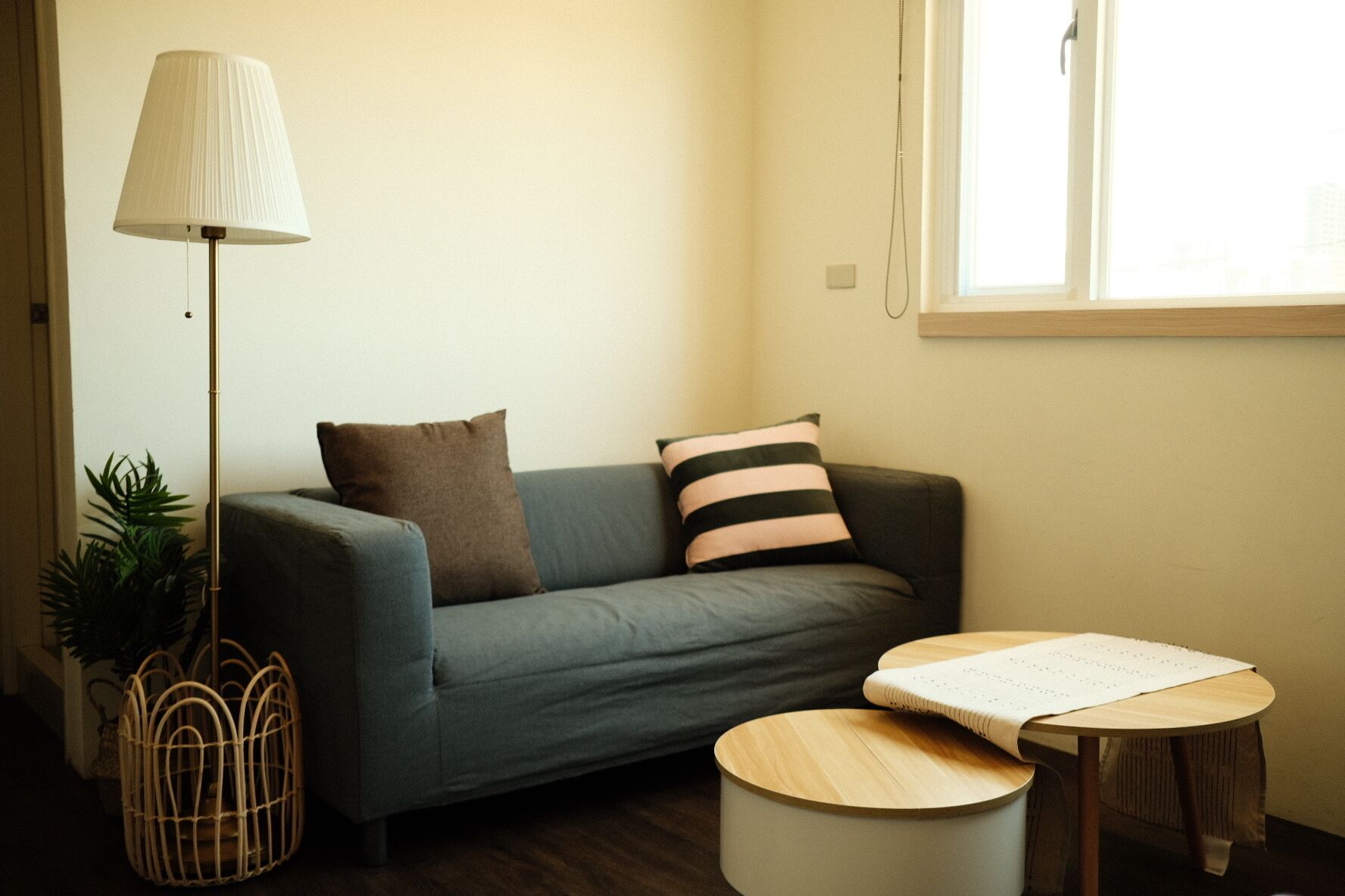 A cozy living room with a grey sofa, a small round table, a floor lamp, and a potted plant.