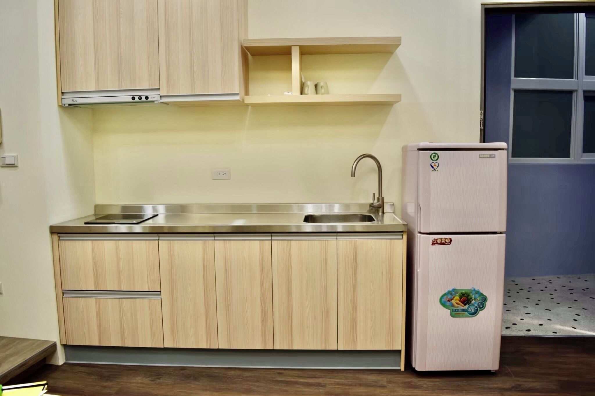 A compact kitchen with wooden cabinets, a stainless steel sink, and a refrigerator.