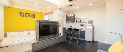 Uma sala de estar moderna com sofá, televisão e área de cozinha com balcão.