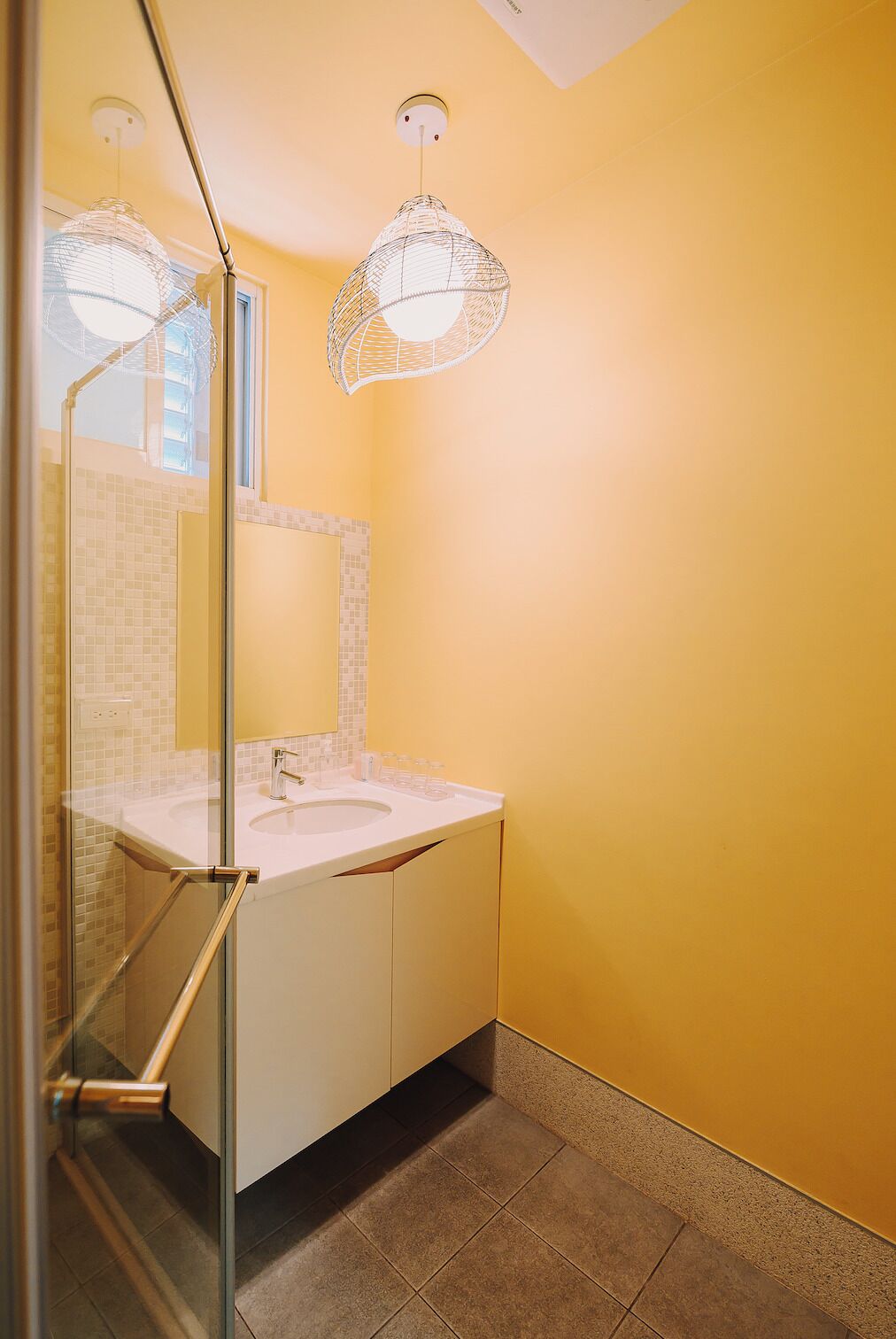 Une salle de bain avec un lavabo blanc, une cabine de douche en verre et un mur jaune.