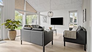 A modern living room with a grey sofa, a smaller armchair, a TV, and a large plant.