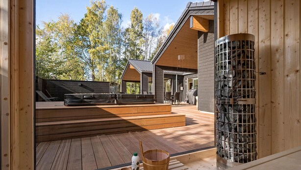 A wooden deck with a sauna, a stone wall, and a view of a house with a covered patio.