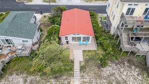 Een strandhuis met een rood dak, een houten terras en een klein veranda met twee stoelen.