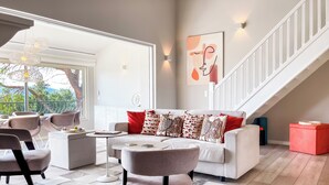 A modern living room with a white sofa, red and patterned cushions, a coffee table, and a staircase with white railings. - Exklusives Ferienhaus mit Traumhaftem Meerblick in Sainte Maxime (Sainte-Maxime)