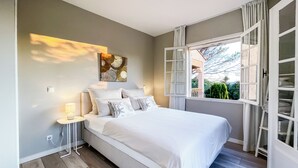 A modern bedroom with a large bed, a bedside table with a lamp, a window with open shutters, and a wall-mounted artwork. - Exklusives Ferienhaus mit Traumhaftem Meerblick in Sainte Maxime (Sainte-Maxime)