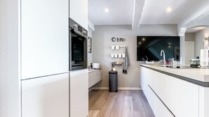 A modern kitchen with white cabinetry, a built-in oven, and a large island with a sink. - Exklusives Ferienhaus mit Traumhaftem Meerblick in Sainte Maxime (Sainte-Maxime)