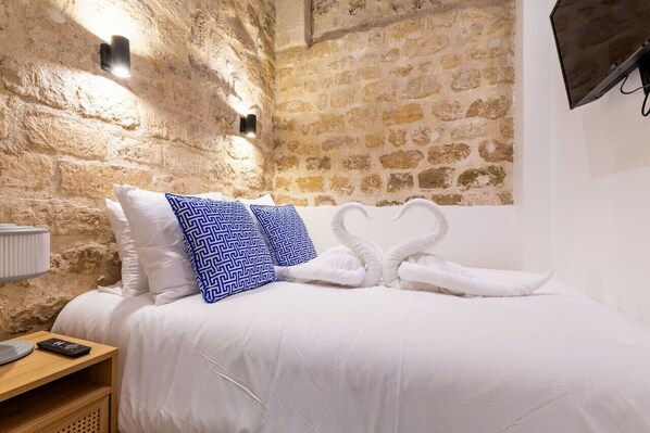 A bed with white bedding, two blue patterned pillows, and two white towels shaped like swans. - Typical Parisian Apart#Quatier Latin#Notre Dame# (Paris)