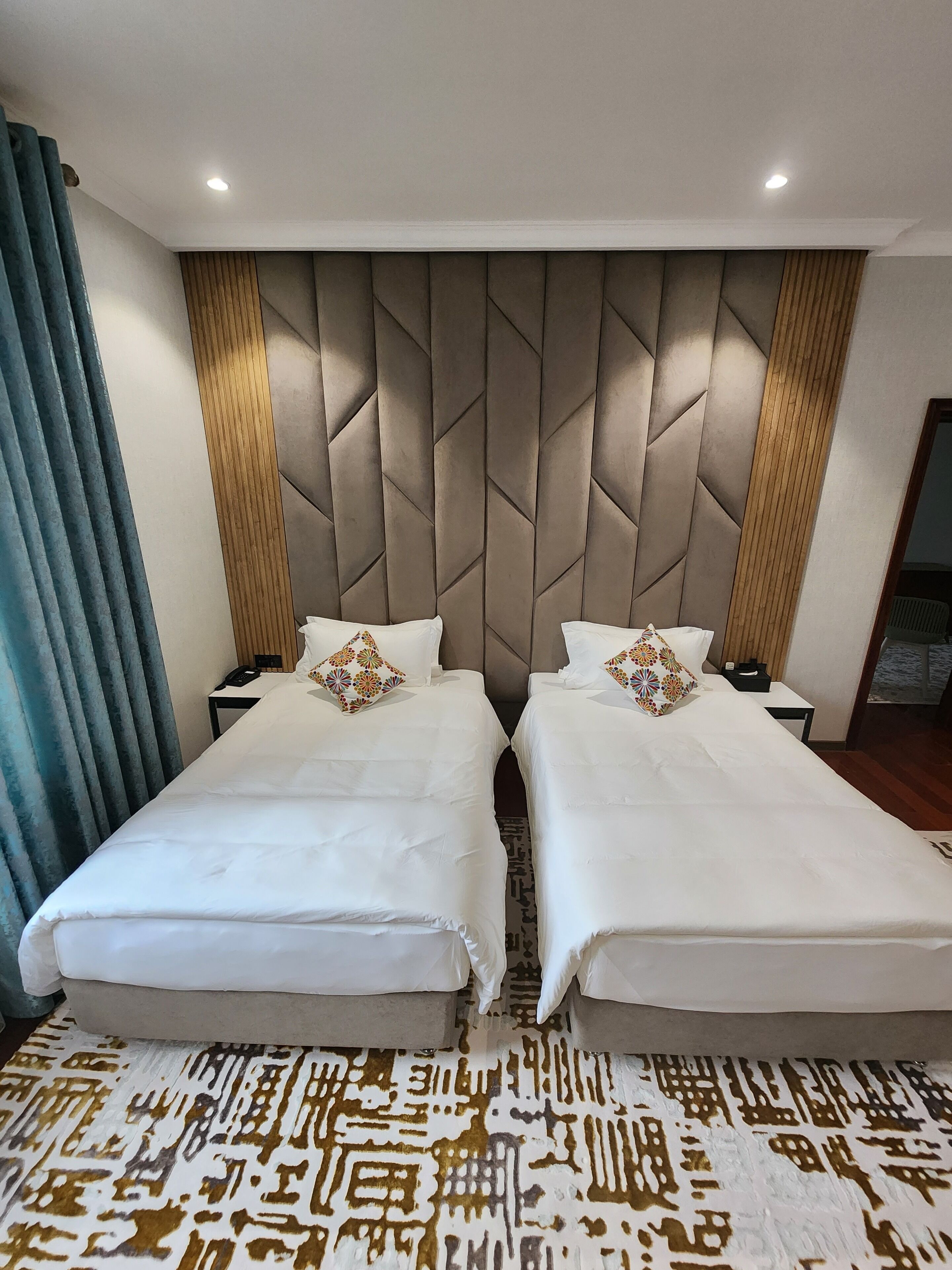 A hotel room with two beds, a patterned carpet, and a modern headboard.