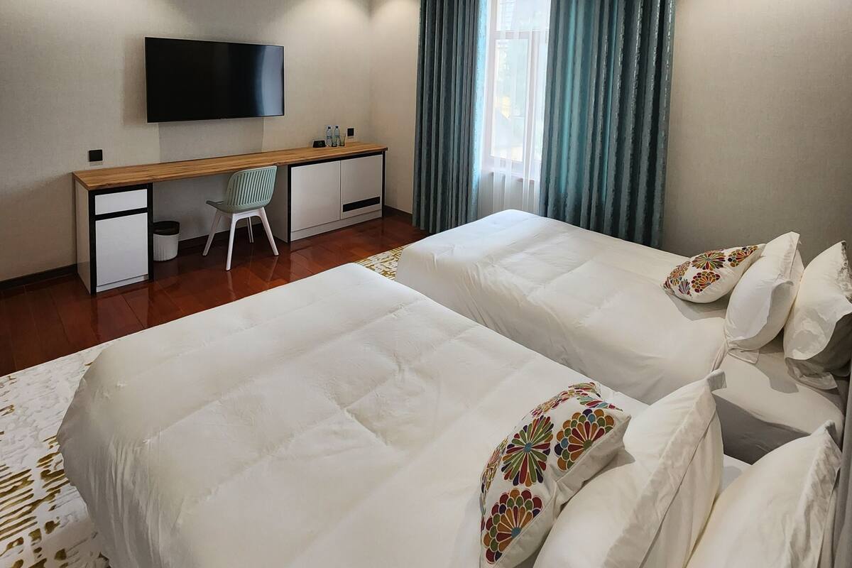 A hotel room with two beds, a desk, a chair, a TV, and a window with curtains.