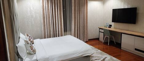 A hotel room with a bed, a desk, a chair, a TV, and an air conditioning unit.