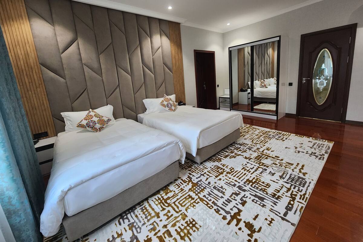 A modern hotel room with two beds, a large mirror, and a patterned rug.