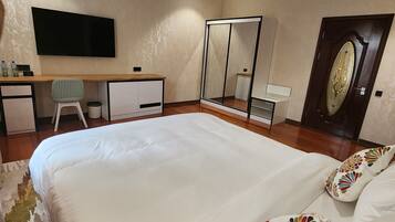 Un dormitorio con una cama grande, un escritorio, una silla, un televisor y un armario.