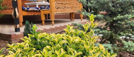 Een traditionele houten bank met ingewikkelde houtsnijwerken, een decoratieve muur en een verzorgde tuin met kleurrijk bladwerk.