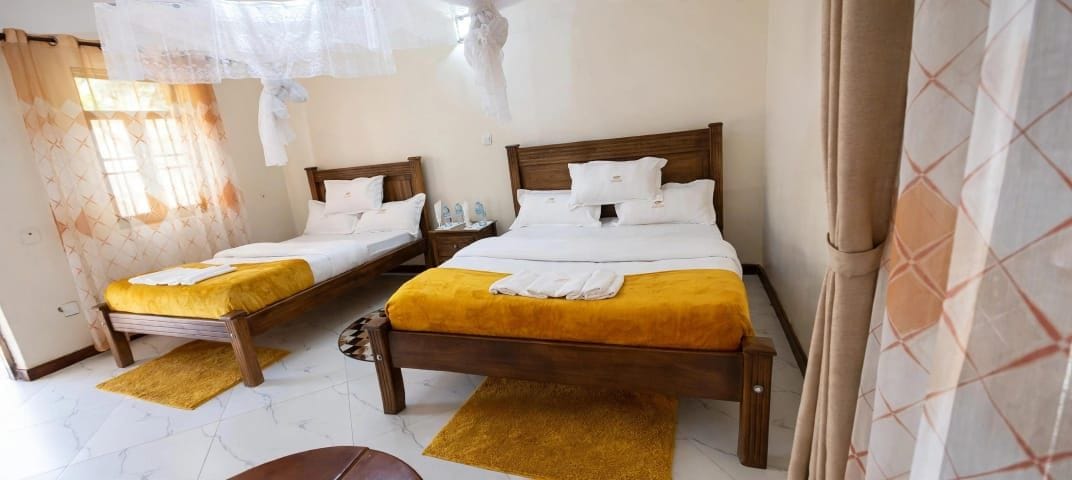 A hotel room with two wooden beds, each with a yellow bedspread and white pillows, a wooden nightstand, and a small table.
