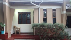 A house with a red and white exterior, a small porch with a wooden chair, and a potted plant. - Montane Safaris Hotel (Fort Portal)