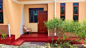 A house with a red exterior, a wooden door, and a small porch with a chair. - Montane Safaris Hotel (Fort Portal)