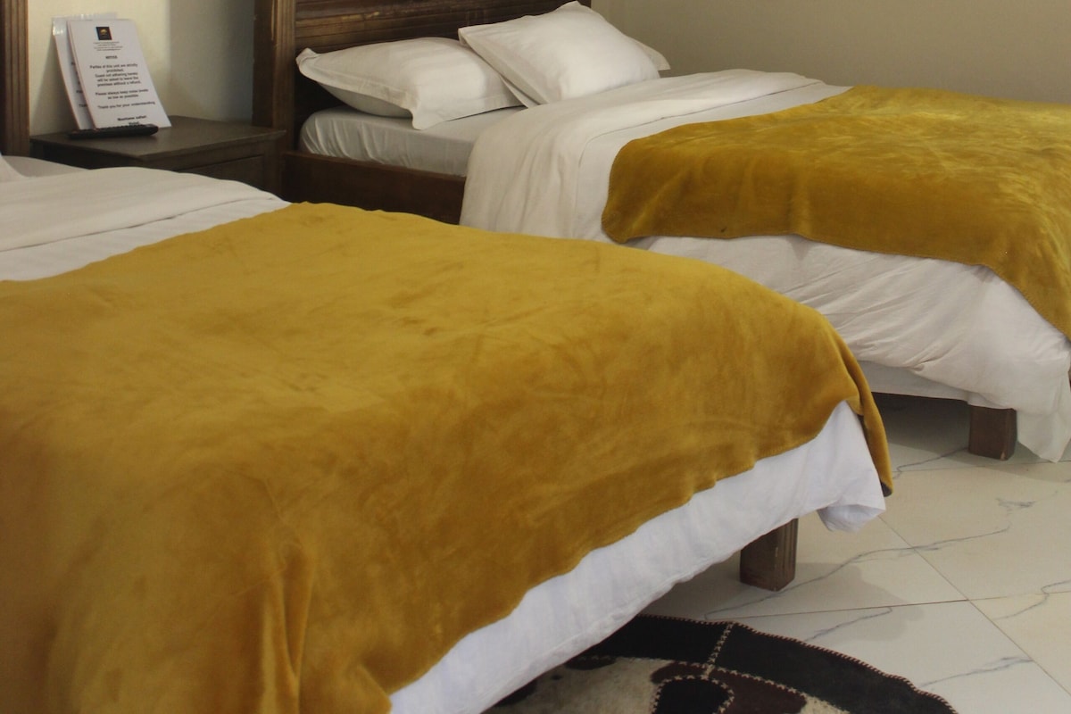A hotel room with two beds, a wooden headboard, a white canopy, and a sign on the nightstand.