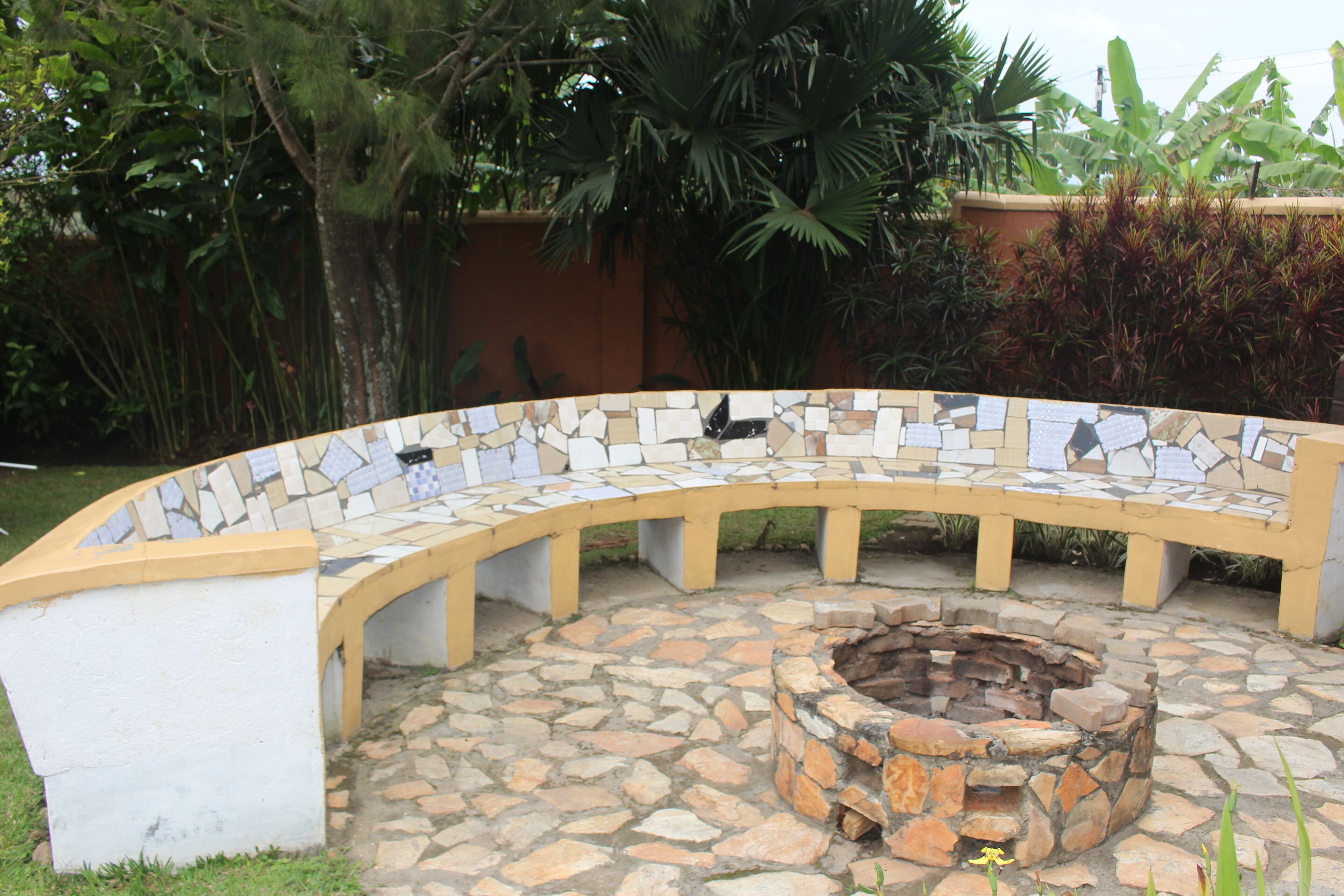 A curved outdoor seating area with a mosaic-tiled bench and a stone fire pit.