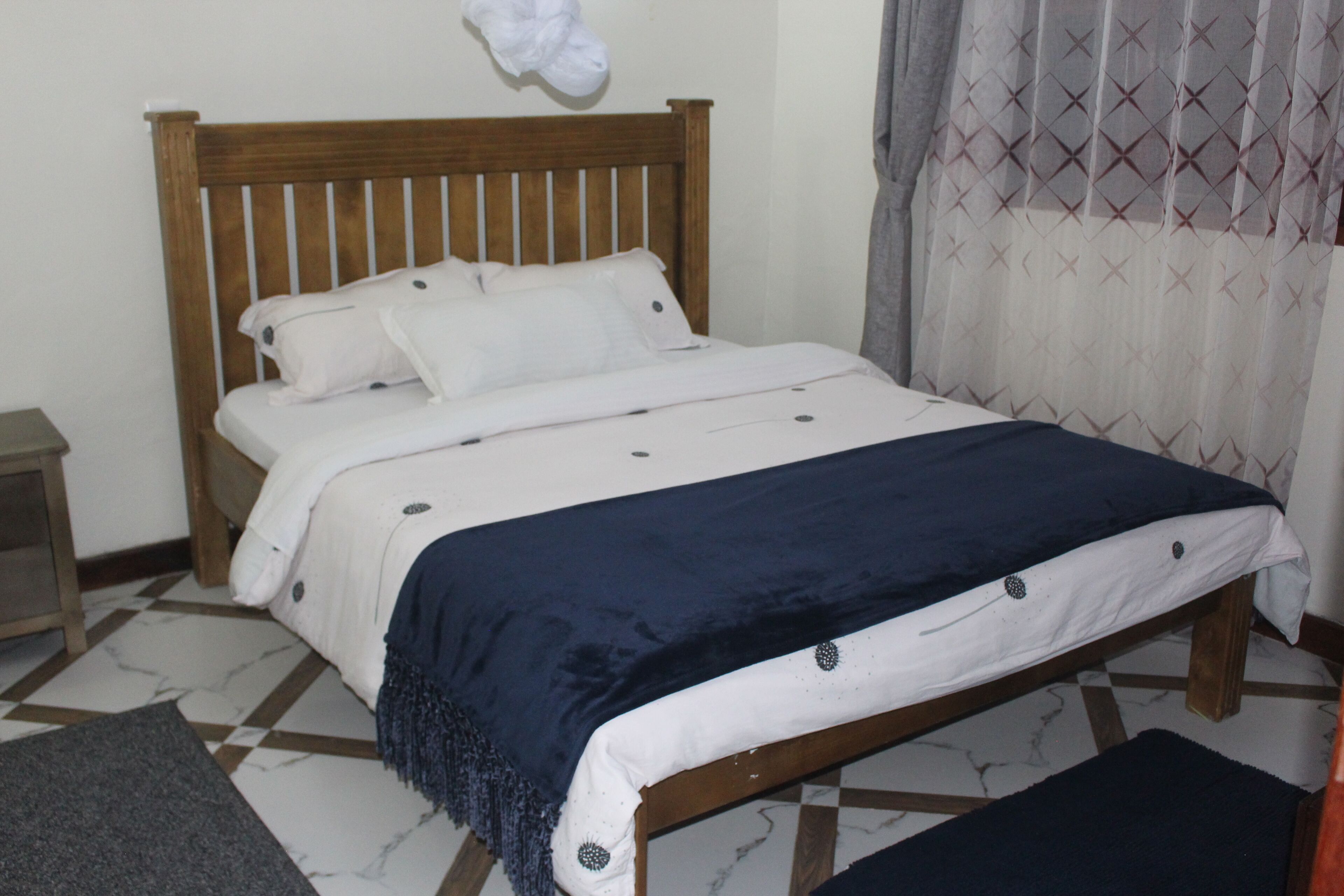 A bed with a wooden headboard, white bedding, and a dark blue throw blanket.
