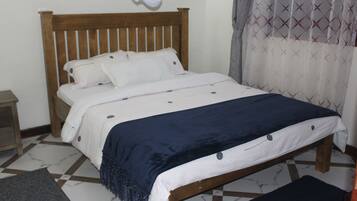 A bed with a wooden headboard, white bedding, and a dark blue throw blanket.
