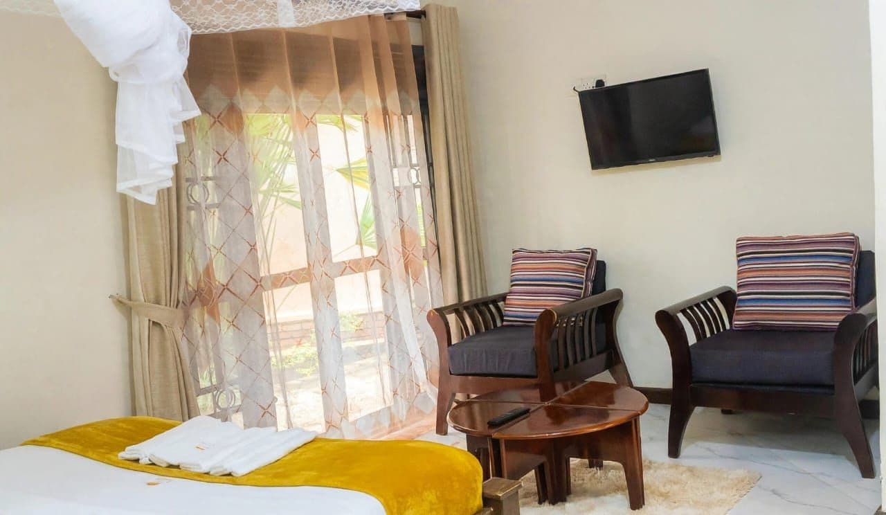 A hotel room with a bed, two armchairs, a small table, a TV, and a window with curtains.