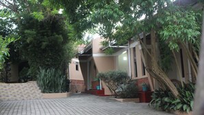 A paved courtyard with a building, trees, and potted plants. - Montane Safaris Hotel (Fort Portal)