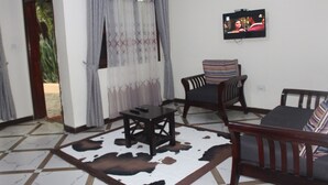 A living room with a television, a sofa, a chair, and a coffee table. - Montane Safaris Hotel (Fort Portal)