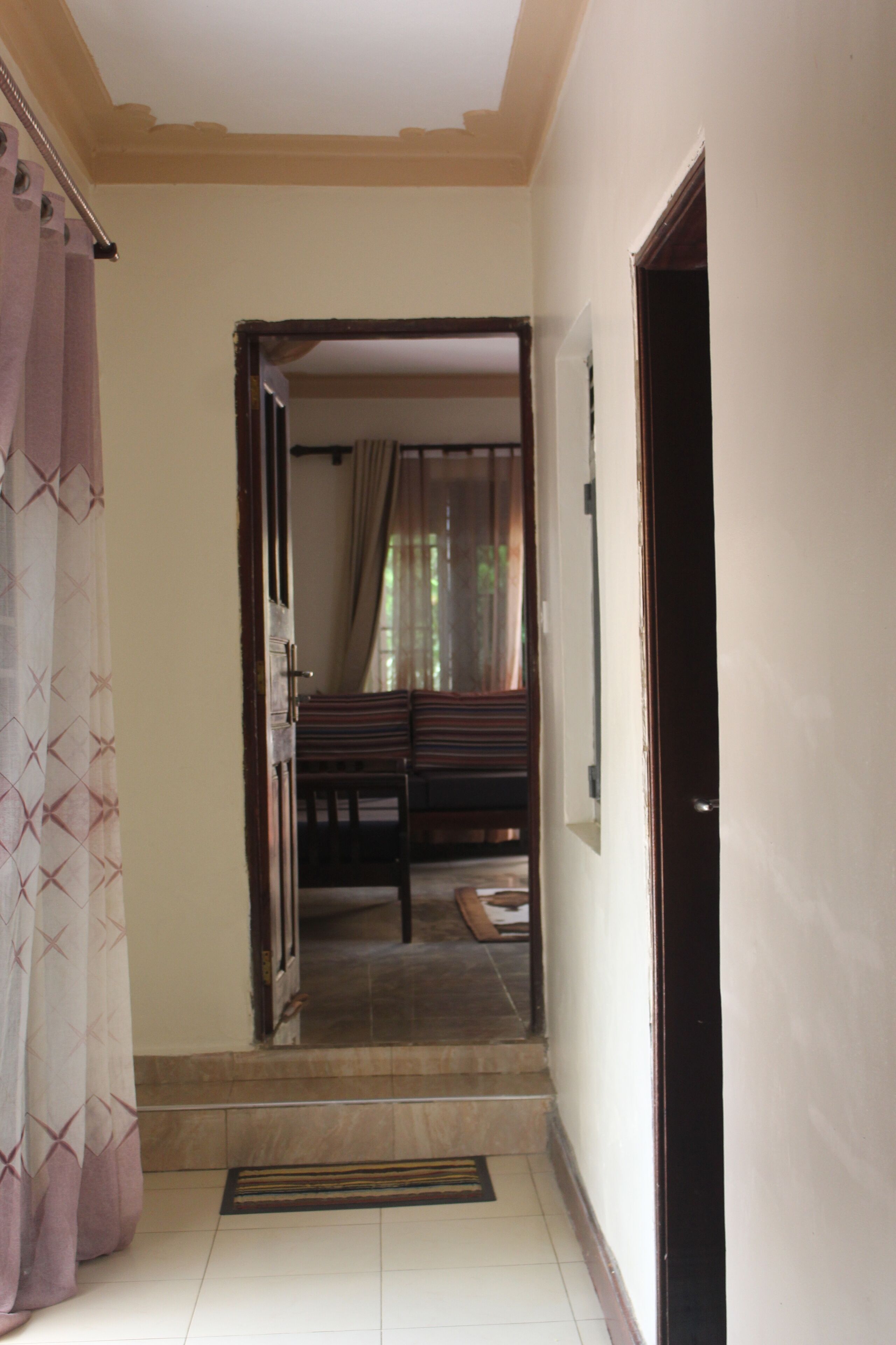 A hallway leading to a bedroom with a bed, a door, and a window with curtains.