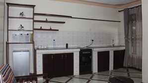 A compact kitchen with a refrigerator, stove, and cabinets. - Montane Safaris Hotel (Fort Portal)