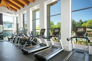 A gym with multiple treadmills and exercise bikes, large windows offering views of greenery and a pool. - TWO CozySuites at Kierland Commons  (Scottsdale)