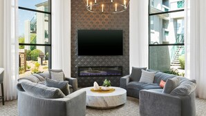A modern living room with a flat-screen TV mounted on a textured wall, two grey sofas, a round coffee table, and a chandelier. - TWO CozySuites at Kierland Commons  (Scottsdale)