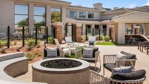 A modern outdoor patio area with seating, a fire pit, and a view of a large house with multiple windows and a covered section. - TWO CozySuites at Kierland Commons  (Scottsdale)
