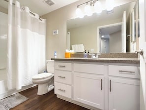 A bathroom with a shower curtain, toilet, sink with countertop, and cabinets. - TWO CozySuites at Kierland Commons  (Scottsdale)