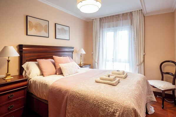 A neatly arranged hotel room with a large bed, two bedside lamps, a chair, and a window with curtains.