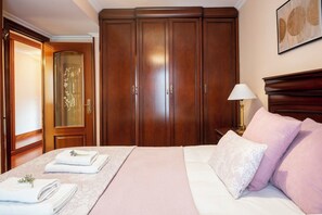 Een hotelkamer met een grote kledingkast, een bed met roze beddengoed en een nachtkastje met een lamp.
