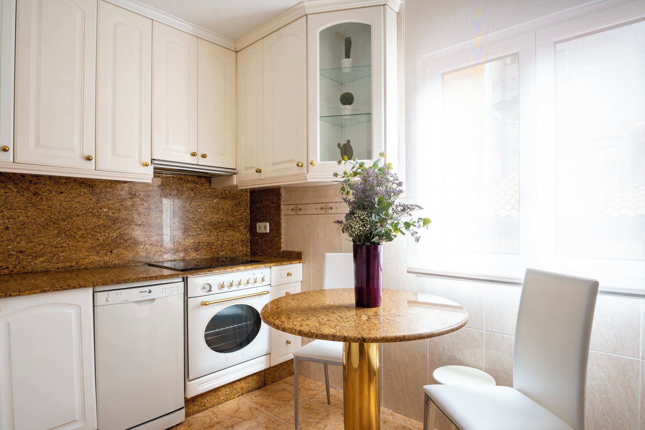 A kitchen with white cabinets, a granite countertop, a built-in oven, and a dining area with a round table and white chairs.