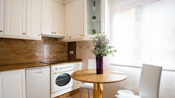 A kitchen with white cabinets, a granite countertop, a built-in oven, and a dining area with a round table and white chairs.
