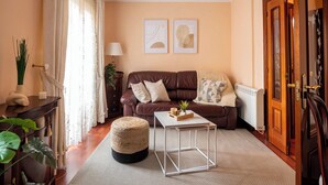 A cozy living room with a brown leather sofa, a small white coffee table, and a wooden side table with a lamp. - Centro y Confort by Wehomes (Santander)