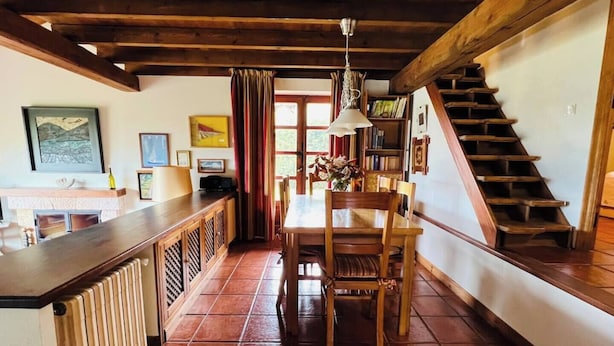 Una cocina con mesa y sillas de madera, una barra y una escalera que sube a otro nivel.