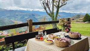 Un conjunto de mesa y sillas de picnic al aire libre, con vistas a la montaña, un florero con flores y diversos alimentos.