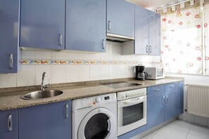 Una cocina con armarios azules, un lavamanos de acero inoxidable, una cafetera, una lavadora y un microondas.