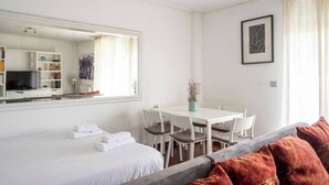 Habitación de hotel con cama, mesa de comedor con sillas, una pequeña planta en maceta y un cuadro en la pared.