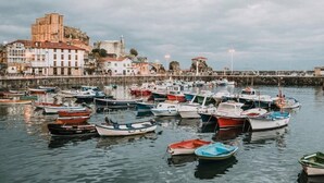 Un port amb nombroses embarcacions amarrades, un edifici històric al fons i una superfície d'aigua tranquil·la.