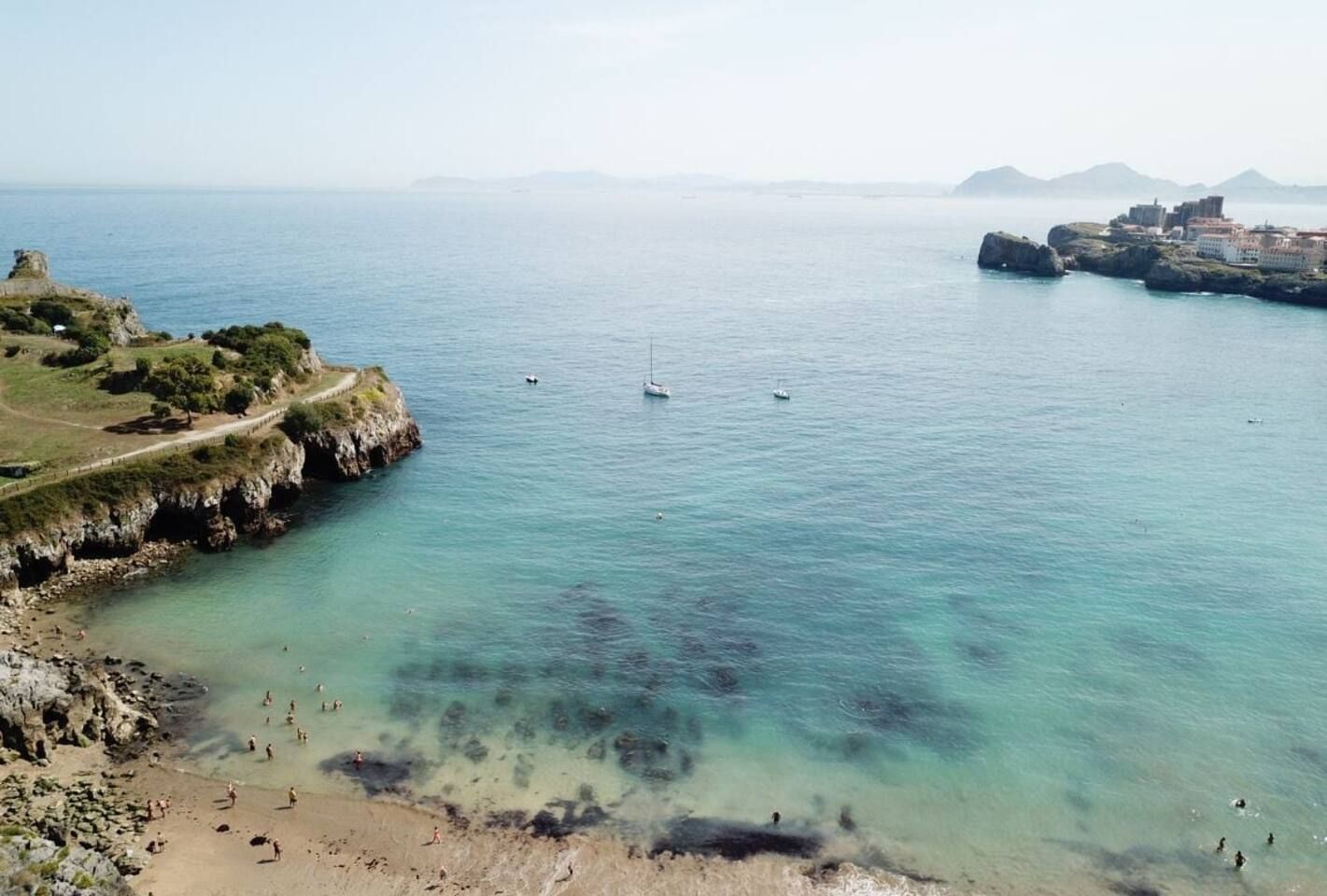 A coastal landscape with a clear beach, rocky cliffs, and a distant town.