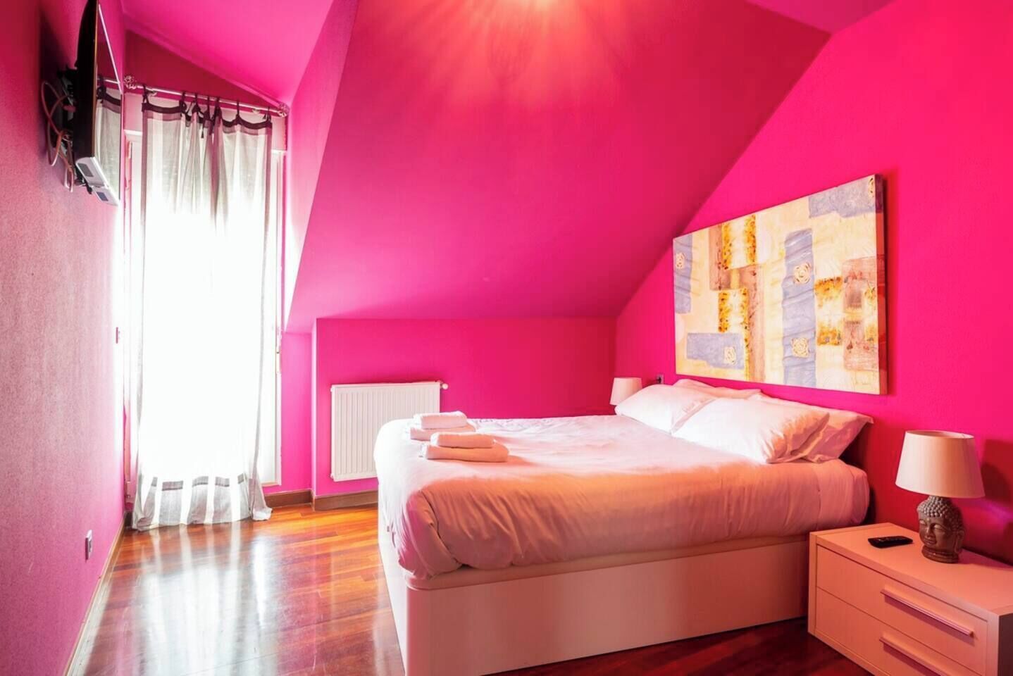 Un dormitorio con una cama grande, una mesita de noche, un radiador y una ventana con cortinas.
