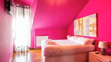 Un dormitorio con una cama grande, una mesita de noche, un radiador y una ventana con cortinas.