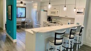 A modern kitchen with white cabinets, a central island with bar stools, and pendant lighting. - Enjoy your beach vacation in this beautifully updated gold rated townhouse!   (Saint Augustine)