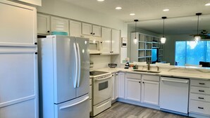 A modern kitchen with white cabinetry, a stainless steel refrigerator, a microwave, and a stove. - Enjoy your beach vacation in this beautifully updated gold rated townhouse!   (Saint Augustine)
