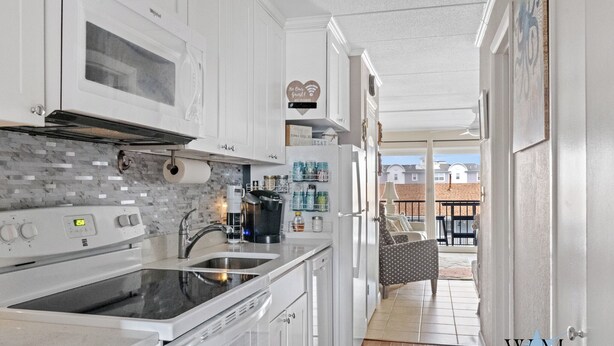 A modern kitchen with white cabinets, a built-in oven, and a coffee maker. There is a view of a patio with a table and chairs. - 1 Bedroom Ocean View Condo with Community Pool (Ocean City)
