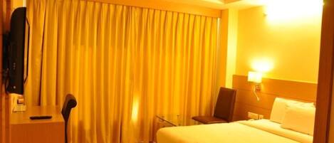A hotel room with a bed, a desk, a chair, a television, and a ceiling fan.